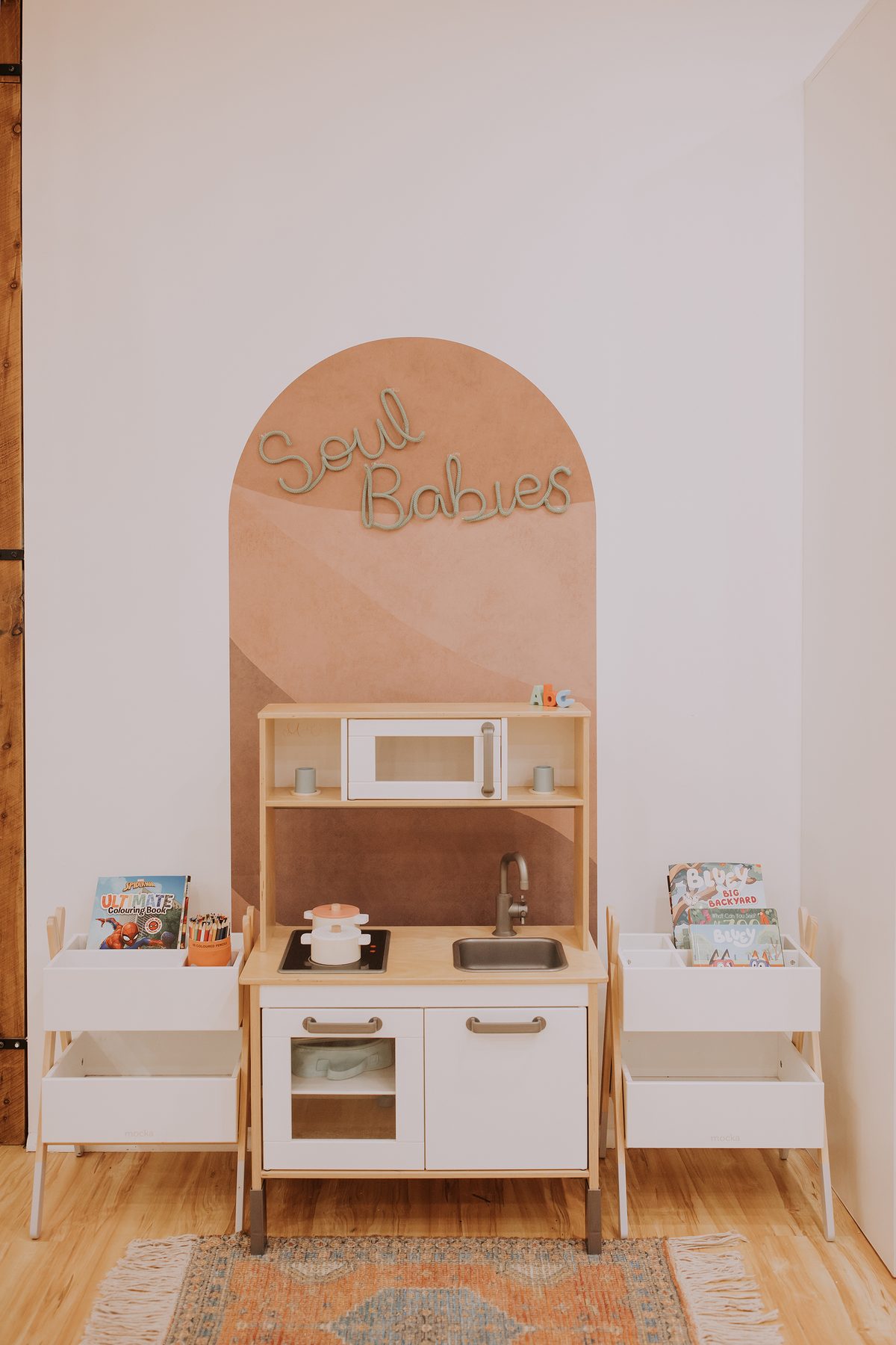 The Soul Babies corner: a terracotta arch on the wall with the name in rope lettering, a wooden play kitchen and two book boxes